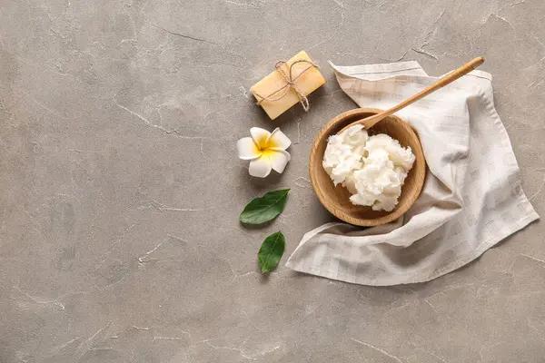 Sabun barlı bir kase Shea yağı ve gri arka planda bir çiçek.
