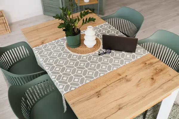 Vazo, ev bitkisi, modern laptop ve masa örtüsü yemek odasındaki ahşap masada.