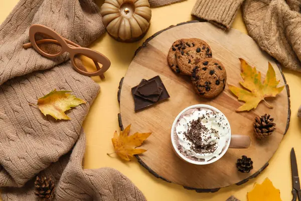 Sonbahar kompozisyonu bir fincan kakao, kazak, ahşap tepsi ve sarı arka planda kurabiyeler.