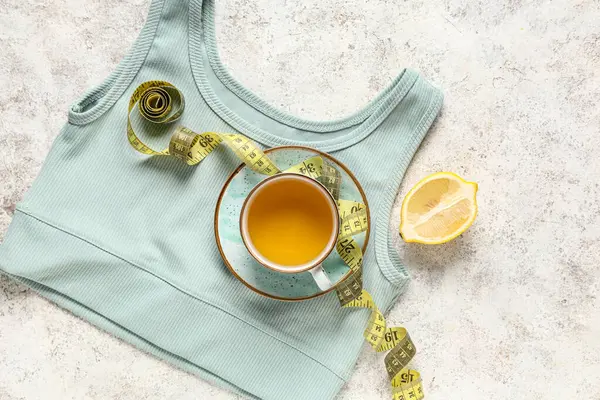 Bir fincan diyet çay, mezura, limon ve arka planda şık spor bluzu. Kilo verme konsepti