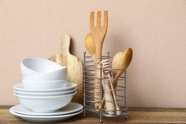 Bej duvarın yanındaki masada mutfak aletleri olan beyaz tabaklar.