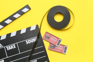 Film makaralı alkışlar ve sarı arka planda sinema biletleri.