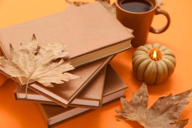 Farklı kitaplar, yanan mum, bir fincan çay ve akçaağaç yaprağı.