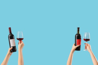 Mavi arka planda kadehleri ve şarap şişelerini tutan kadın eller.