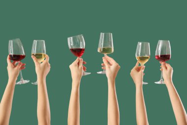 Yeşil arka planda farklı şarapların kadehlerini tutan kadın eller.