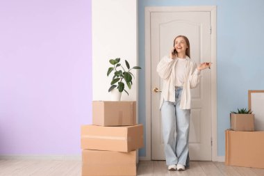 Anahtarları ve karton kutuları olan güzel genç bir kadın taşınma gününde telefonla konuşuyor.