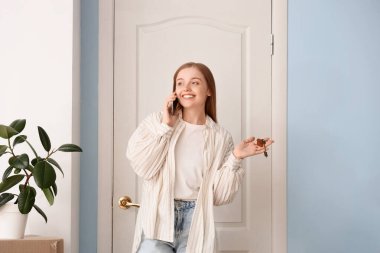 Anahtarları olan güzel genç bir kadın taşınma gününde telefonla konuşuyor.