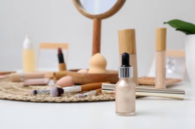 Işık masasında bir şişe serum, dekoratif kozmetik ve makyaj malzemesi.