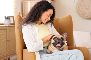 Güzel bir Afro-Amerikalı kadın, sevimli bir Fransız buldoguyla evdeki koltukta oturuyor.