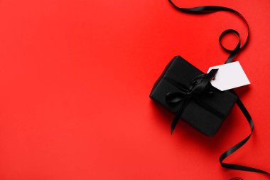 Kırmızı arka planda boş karton etiketli ve kurdeleli hediye kutusu. Kara Cuma indirimi