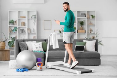 Evde koşu bandında cep telefonu eğitimi almış genç bir adam.