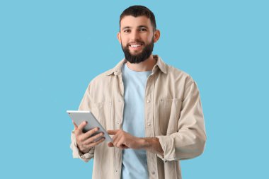 Mavi arka planda tableti olan yakışıklı, mutlu bir adam.