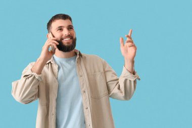 Yakışıklı genç adam mavi arka planda cep telefonuyla konuşuyor.