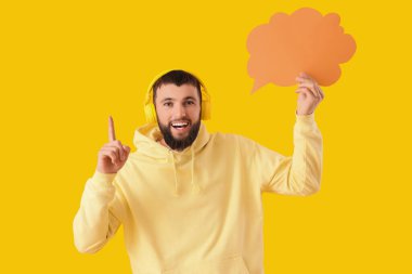 Sarı arka planda boş konuşma balonu olan kulaklıklı yakışıklı genç adam.