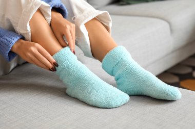 Sıcak mavi çoraplı bir kadın evdeki kanepede oturuyor, yakın plan.