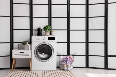 Modern çamaşır makinesi, komodin ve sepet çamaşır odasında katlanan ekranın yanında.