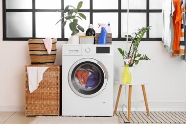 Çamaşır makinesi, sepeti ve elbise askısı olan çamaşır odasının içi.