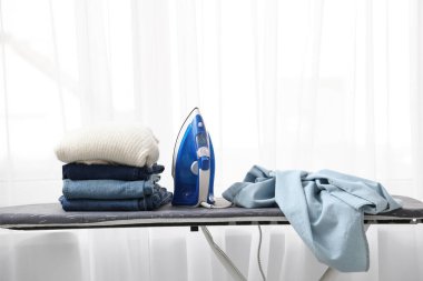 Odanın penceresinin yanında elektrikli ütü ve giysi bulunan tahta.