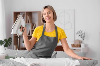 Önlüklü güzel bir kadın evde giysilerini ütülüyor.