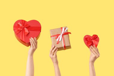 Sarı arka planda farklı hediye kutuları olan kadın elleri. Sevgililer Günü kutlaması