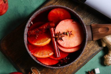 Elmalı, portakallı ve yeşil arka planda farklı baharatlı sıcak şarap tenceresi.