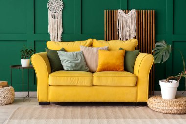 Yeşil duvarın yanında rahat sarı kanepesi ve çiçekleri olan şık bir oda.