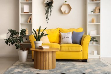 Rahat sarı kanepesi, sehpası ve raf ünitesi olan şık bir oda.