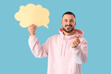 Konuşma baloncuğu olan yakışıklı genç adam mavi arka planda kalp hareketi gösteriyor.