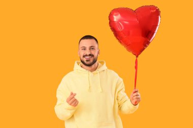 Kalp şeklinde balonu olan yakışıklı genç adam sarı arka planda kalp hareketi gösteriyor.