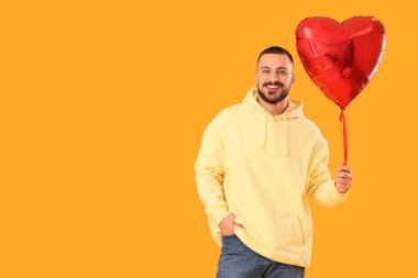 Sarı arka planda kalp şeklinde balonu olan yakışıklı genç adam.