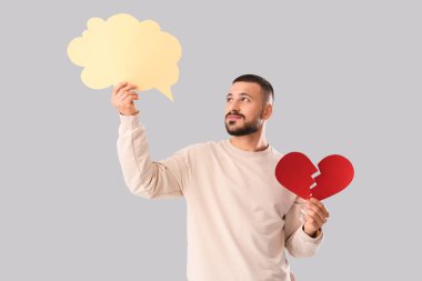 Kırık bir kalbi ve gri arka planda konuşma balonu olan düşünceli yakışıklı genç bir adam.