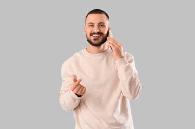 Yakışıklı genç adam cep telefonuyla konuşuyor ve gri arka planda kalp hareketi gösteriyor.