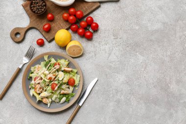 Lezzetli tavuklu Sezar salatası, domates, limon ve gri arka planda bir kase biber.