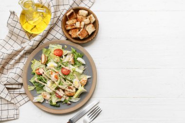 Lezzetli tavuklu Sezar salatası ve beyaz ahşap arka planda bir kase kızarmış ekmek.
