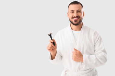 Beyaz arka planda tıraş bıçağı olan bornozlu genç bir adam.