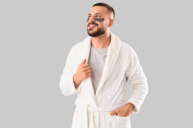 Gri arka planda göz bantları olan, bornozlu, gülümseyen genç adam.