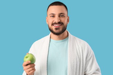 Mavi arka planda yeşil elmalı bornoz giyen genç adam.