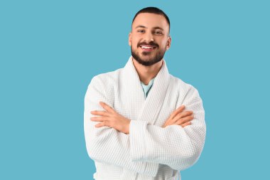 Mavi arka planda çapraz kollu cüppeli genç adam.