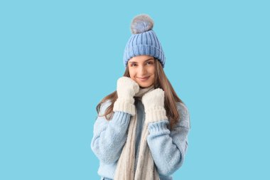 Mavi arka planda şık, sıcak giysiler içinde güzel genç bir kadın.