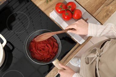 Kızartma tavasında domates ezmesi karıştıran genç bir kadın. Mutfakta kaşıkla.