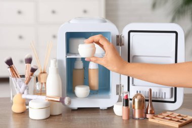 Beyaz duvarın yanındaki küçük kozmetik buzdolabından krema alan kadın eli. Yakın çekim.