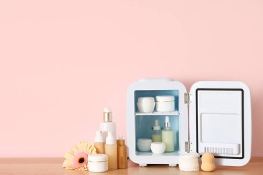 Kozmetik ürünleri ve pembe arka planda çiçek olan küçük bir buzdolabı. Yakın çekim.
