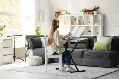 Oturma odasında sentezleyici çalan kulaklıklı ve not kağıtlı genç bir kadın.