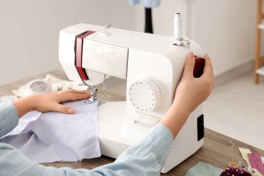 Atölyedeki masanın yanında dikiş makinesi kullanan genç bir terzi.