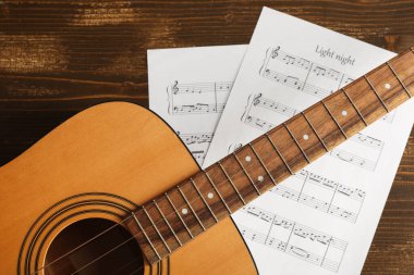 Ahşap arka planda müzik kağıtları ve gitar, yakın plan