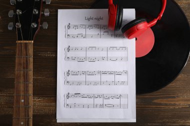 Müzik sayfası, vinil disk, modern kulaklık ve gitar ahşap arka planda, yakın plan