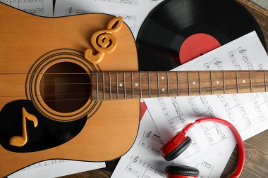 Gitar, müzik kağıtları, kulaklıklar ve plak diski ahşap masada, yakın plan.
