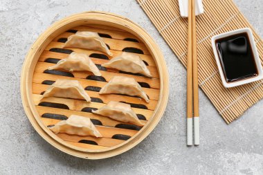 Lezzetli Japon gyoza 'lı bambu buharı ve gri arka planda bir kase soya sosu.
