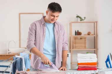 Evde ütü yapan bir yığın temiz elbisesi olan yakışıklı genç adam.