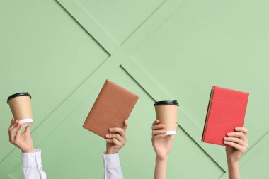 Kitaplı kadın eller ve yeşil arka planda kağıt bardaklar.